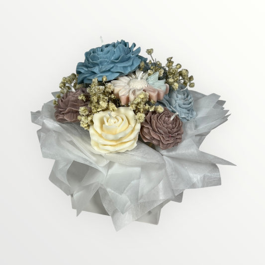 Kukkakimppu kynttilöistä – sinisiä, beigejä ja pastellisia kukkakynttilöitä valkoisella silkkipaperilla pakattuna.