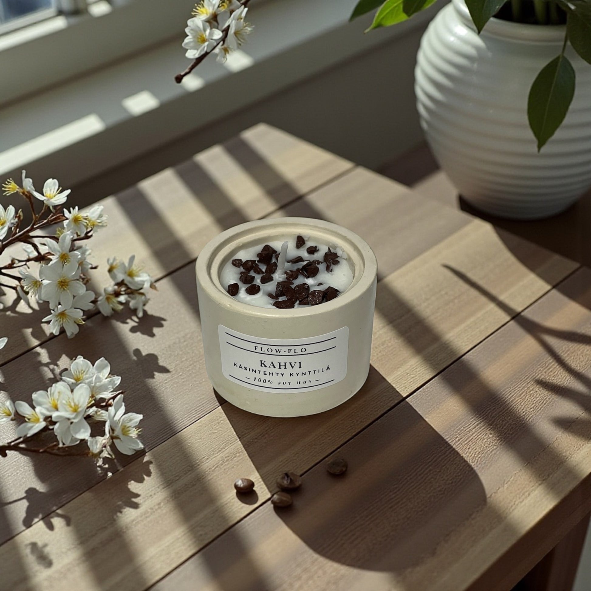 Flow Flo Kahvi kynttilä käsintehdyssä kipsipurkissa, kahvipapuja ja kukkia taustalla – suomalainen käsintehty soijavahakynttilä
