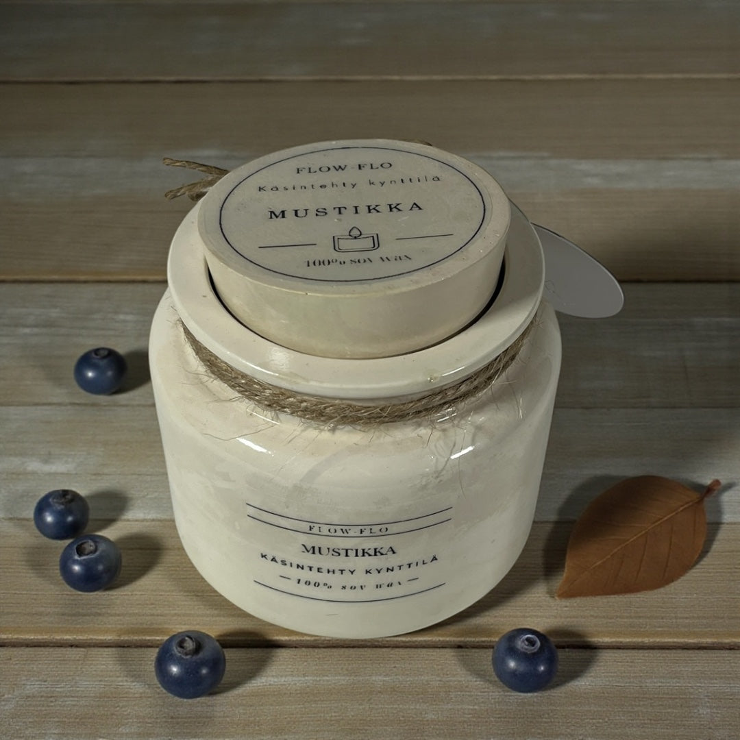 Flow Flo Mustikka käsintehty tuoksukynttilä valkoisessa rustiikkisessa purkissa juuttinarukoristeella, tuoreita mustikoita ympärillä puupöydällä – raikas ja mehukas marjainen ekologinen soijavaha kynttilä sisustukseen.