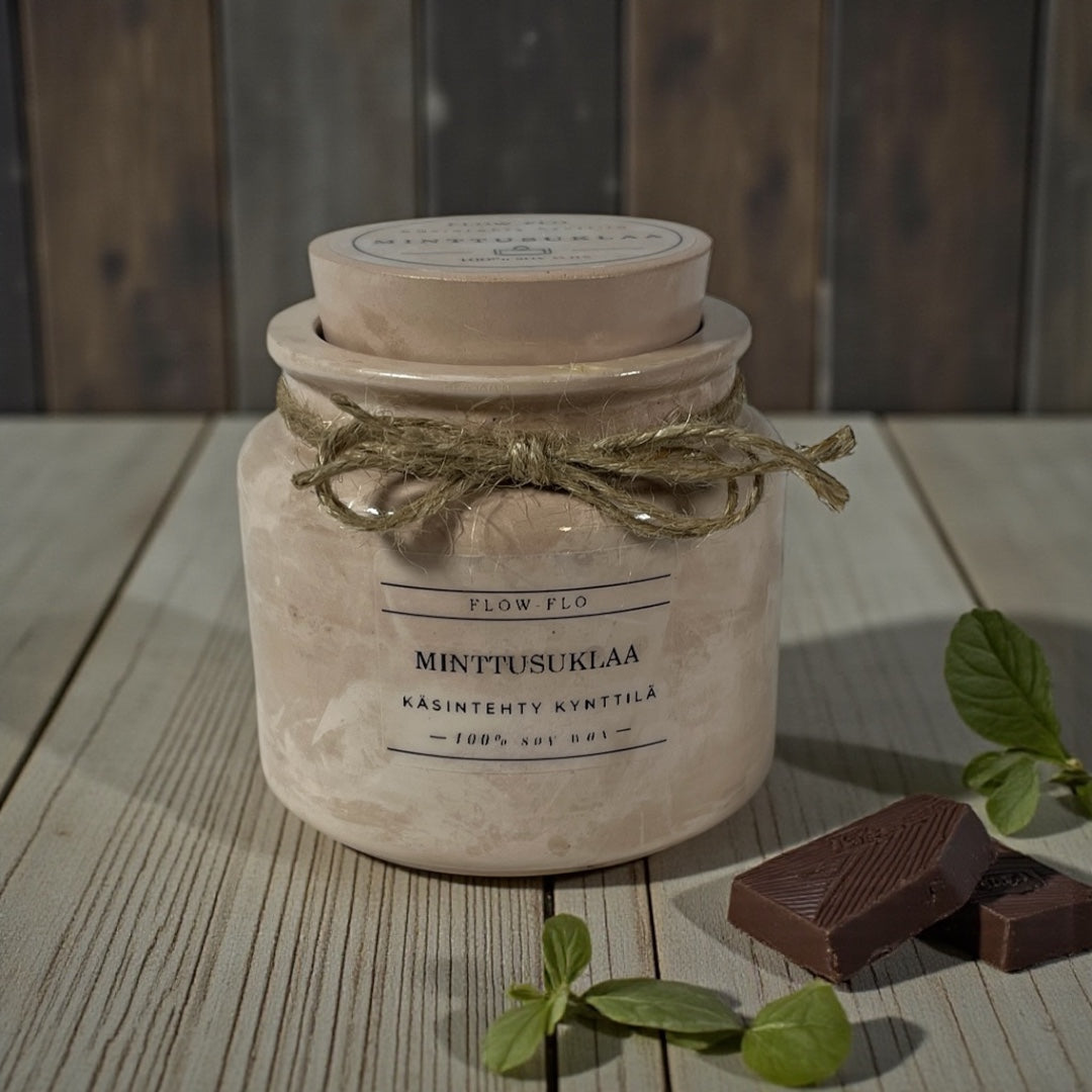 Flow Flo Minttusuklaa käsintehty tuoksukynttilä vaaleanruskeassa rustiikkisessa purkissa juuttinarukoristeella, tuoreita mintunlehtiä ja tummaa suklaata ympärillä – raikas ja makea ekologinen soijavaha kynttilä sisustukseen.