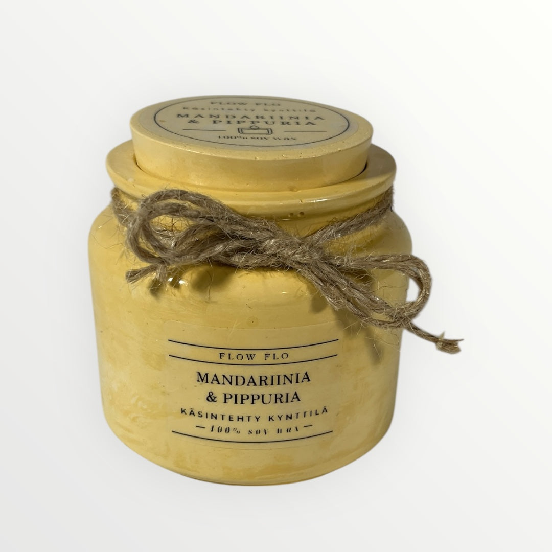 Flow Flo Mandariini & Pippuri -käsintehty tuoksukynttilä vaaleankeltaisessa rustiikkisessa purkissa narukoristeella, tuoreita mandariiniviipaleita ja mustapippureita ympärillä – raikas ja mausteinen ekologinen soijavaha kynttilä