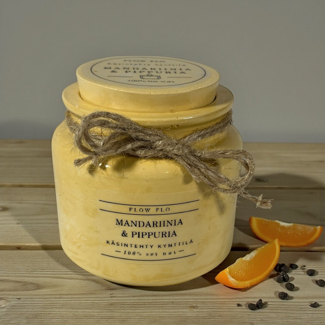 Flow Flo Mandariini & Pippuri käsintehty tuoksukynttilä vaaleankeltaisessa rustiikkisessa purkissa narukoristeella, tuoreita mandariinilohkoja ja mustapippureita ympärillä – raikas ja mausteinen ekologinen soijavaha kynttilä sisustukseen.