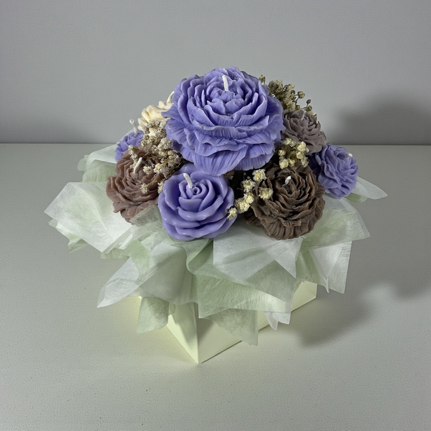 Kaunis kynttiläkimppu pöydällä: lila, beige ja ruskeat pionikynttilät tulitikkurasian vieressä